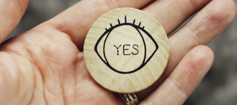 A small wooden disc with the word yes on it, held in the palm of a woman's hand.