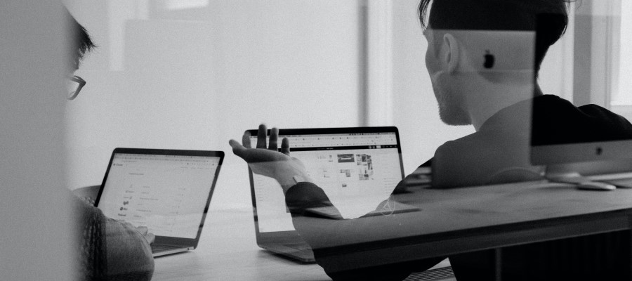 Block and white of two colleagues with laptops in discussion, through a glass window with a reflection