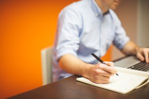 Man in blue shirt on orange background making notes in a notebook